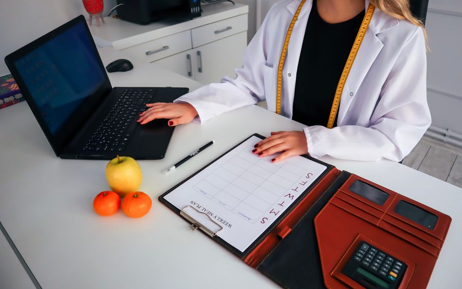 Dietitian working on meal plan with laptop, fruits, and calendar for health consultation.