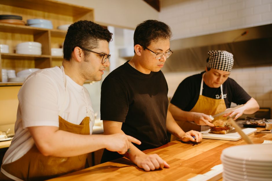 Three chefs working together at a kitchen counter, preparing dishes with focus and teamwork.